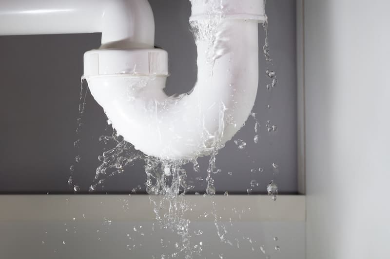Water leaking and splashing from a white plumbing pipe under a sink